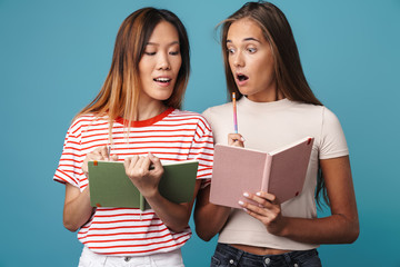 Portrait of surprised women holding exercise books and peeking