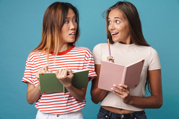 Portrait of surprised women holding exercise books and looking at each