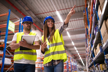 Shot of positive cheerful warehouse workers checking inventory on shelves together and controlling...