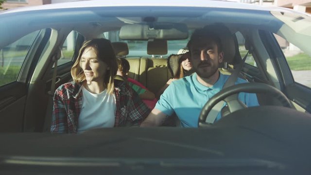 Cheerful Young Family Driving In Car Through Modern City. Front View Of Parents And Children Traveling Together Having A Nice Summer Journey By Car.