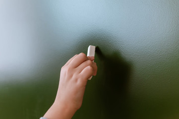 schoolboy hand writes in chalk on a blackboard during a lesson at school.