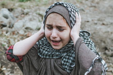a refugee child in the war, a Muslim girl with a dirty face on the ruins, the concept of peace and war, the child is crying and waiting for help. - obrazy, fototapety, plakaty