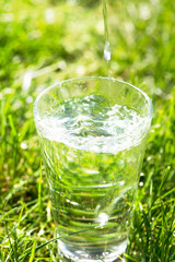 A glass of clean transparent drinking water on a grass background.