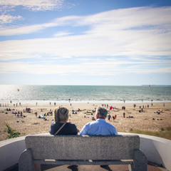 couple assis de dos face à l'océan et une plage avec du monde en Loir atlantique à Saint Michel...