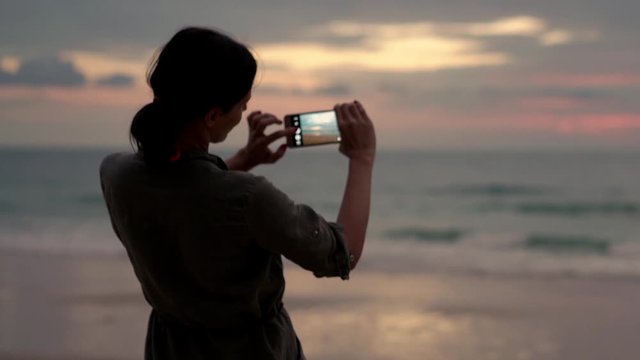 Silhouette of woman doing selfie photo with cellphone during sunset