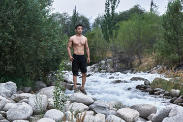 Kazakh muscular athlete man trains and exercises by the river in nature. Asian handsome does extreme fitness workout outdoors