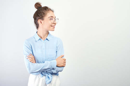 Portrait of Asian Kazakh student girl with bun of hair on head and glasses with arms crossed smiling and looking to the side with copy space on white background