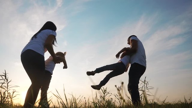happy family teamwork a mom and daddy is circling a little daughters hands hold hand plane flight side to side slow motion video. father and little boy plays lifestyle running sunset silhouette hands