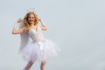 Little goddess with white wings alone on blue sky background. Teenager happy angel. Portrait of little curly blond Angel girl.