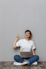 Image of young woman pointing finger upward while sitting with laptop