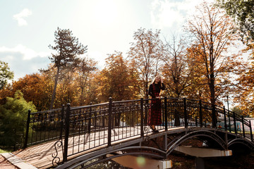 Girl on bridge with Scottish long red dress. Girl with long brown hair in autumn park.