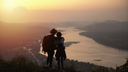 couple backpacker standing on cliff with sunset background