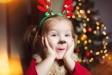 cute funny baby is very surprised. pretty girl in a fancy dress deer on the background of the...