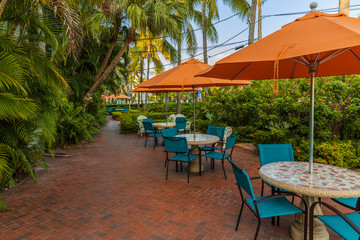 Beautiful view of outdoor tables. Blue chairs and orange umbrellas on green palm trees and blue sky background. Key West, Florida. USA. 