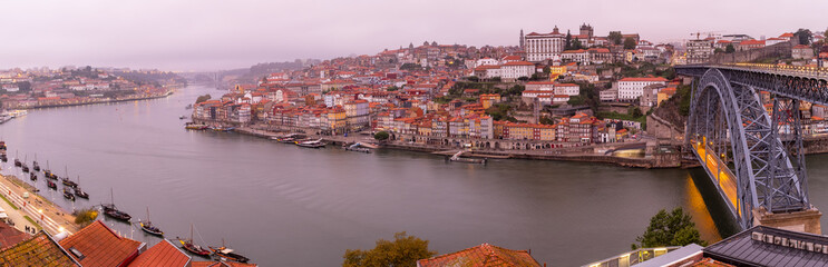 Panoramic view of the Douro River snaking through the city of Porto with the Ponte Luiz bridge in the foreground with traditional boats tied up on the river taken at dawn