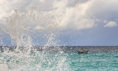 Crushing waves against a cloudy sky and a small fishing boat under bad weather conditions