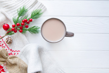 Fototapeta na wymiar White woolen sweater with christmas ornament and a cup og hot cacao on white wooden background. Christmas red decoration. Space for greeting, copy space. 