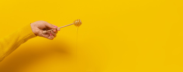 honey dripping from honey dipper on yellow background. Thick honey dipping from the wooden honey...