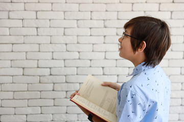 cute and smart boy holding books and wearing glasses looking and thinking of something while smiling