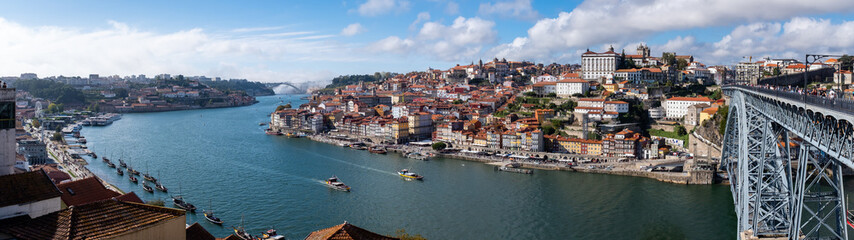 Naklejka na ściany i meble Panoramic view of the Douro River, snaking through the city of Porto with the Ponte Luiz bridge in the foreground and traditional boats tied up on the river.
