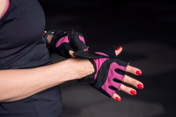 Closeup of woman putting on workout gloves with no brand logo over manicured hands with bright red nail polish on black background