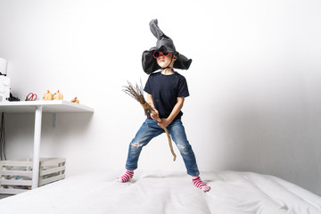 A little boy in a black witch hat and pink glasses holds a broom.