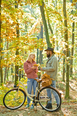 Young hipster couple having a romantic date in the forest standing one against the other near bike. First really serious relationship. First date. Romantically involved.