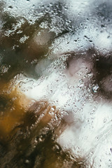 Fototapeta premium Blurred reflection of the street in a misted window, drops of water after rain flow down the glass. Water drops on window. Rainy mood concept.