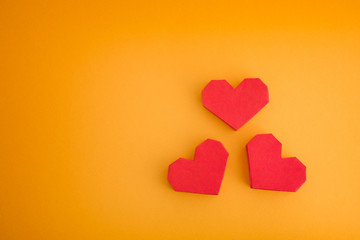 Three red origami hearts on a yellow background