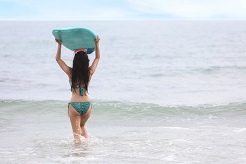 Fototapeta premium rear view sexy surfer asian girl holding green surfboard on tropical sea in green swimsuit on sandy beach on summer time. (water sport or vacation holiday concept)