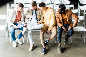 four young multicultural businessmen discussing startup project while sitting in conference hall