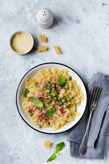 Fettuccine pasta with bacon and green peas and parmesan cheese in light plate on old gray concrete background. Top view.