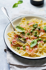Fettuccine pasta with bacon and green peas and parmesan cheese in light plate on old gray concrete background. Top view.