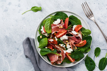 Spring Salad with spinach, cherry tomato, mozzarella, pine nuts and ham with olive oil in a simple ceramic plate on an old concrete gray background.