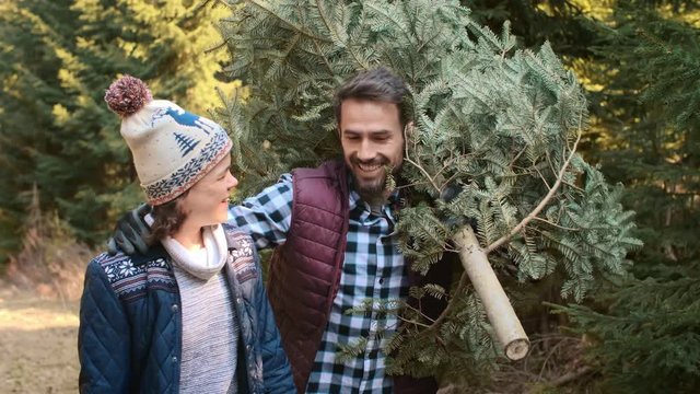 Smiling dad and teenage son carrying big christmas tree
