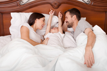 family and morning concept - happy child with parents waking up in bed at home