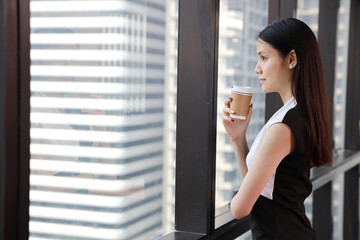 side view of asian businesswoman or lawyer in black and white dress with confident face who standing and holding cup of coffee in office and look away with city view background