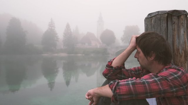 Lonely upset distraught man at lake pier in foggy morning