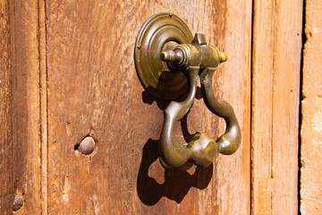 Obraz premium Close up of antique metal iron door knocker on old wood entrance in bright natural sun light - Provence, France