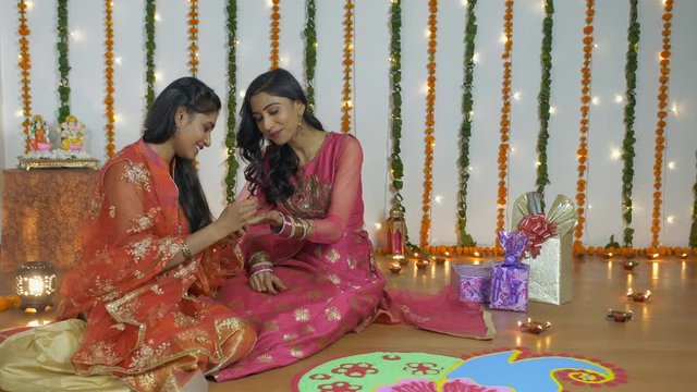 Beautiful mehndi artist painting hands of a female on the occasion of Diwali - the festival of India. Young girl applying designer mehndi in the hands of her sister with a decorative festive backgr...