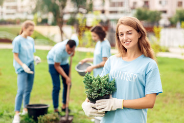 Volunteering. Young people volunteers outdoors planting trees girl standing with pot close-up looking camera smiling happy blurred background