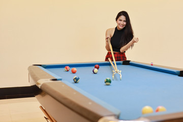 Fototapeta premium beautiful and sexy asian woman in black dress playing billiard or snooker on blue pool table with happy smiling face during holiday vacation