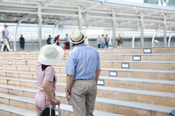 asian traveler couple husband and wife in pink and blue shirt with white nice hat and luggage walking in downtown, he pointing something with left copy space