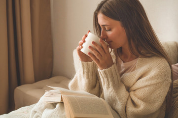 Cozy Autumn winter evening. Woman drinking hot tea and reading book. 