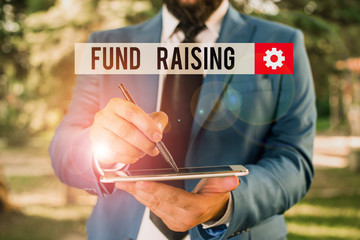 Text sign showing Fund Raising. Business photo showcasing the act of seeking to generate financial support for a charity Businessman in blue suite stands with mobile phone in hands