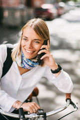 Fototapeta premium Beautiful young woman posing with her bicycle while using phone