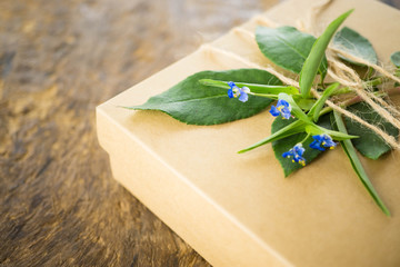 Close up  brown hand craft gift box with green leaves and spring floral on wood background.