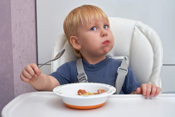 Three year old boy eats from a plate with a spoon