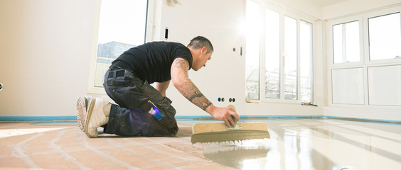 männliche Arbeitskraft, die mit selbstnivellierendem Zementmörtel während der Bodensanierung...