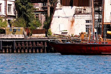 Fototapeta na wymiar Red ship stands at the pier in a small town surrounded by houses and greenery